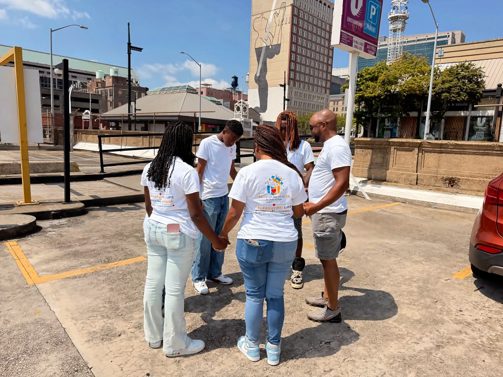 Birthday 2 Remember volunteers standing in a prayer circle, holding hands before an outreach in downtown Atlanta.
